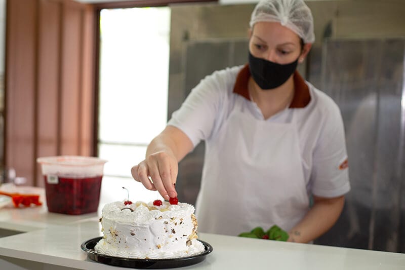 Mulher colocando a cereja em cima da torta da Confeitaria Helena