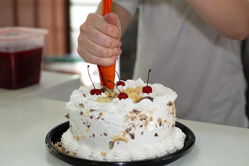 Mulher finalizando a cobertura da torta da Confeitaria Helena