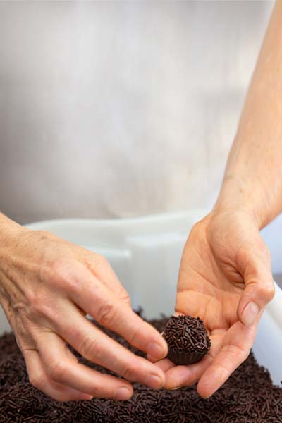 Mulher enrolando um docinho de brigadeiro da Confeitaria Helena