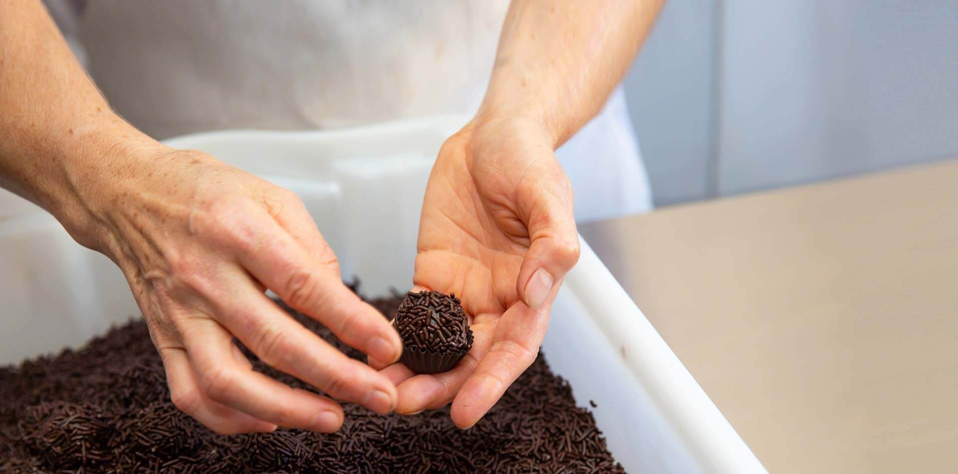 Mulher enrolando um docinho de brigadeiro da Confeitaria Helena